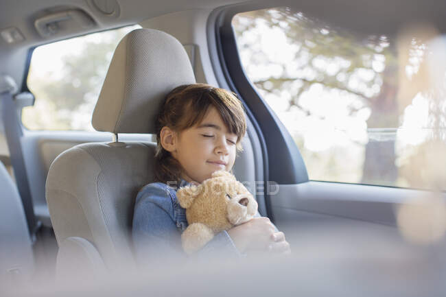Девушка с плюшевым мишкой спит на заднем сидении машины — стоковое фото