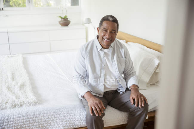 Retrato de un hombre mayor sonriente sentado en la cama - foto de stock