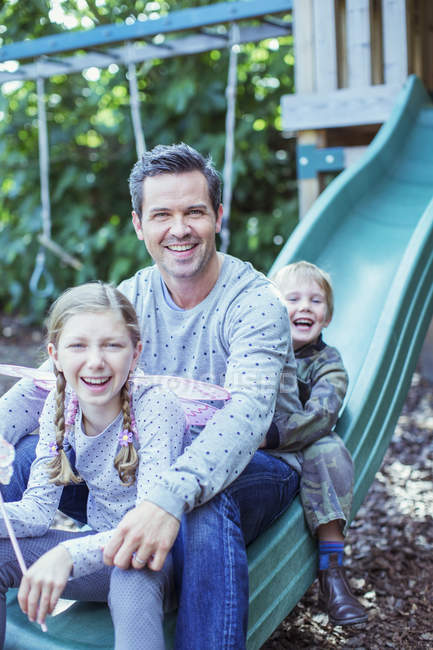 Father and children sitting on slide — Stock Photo