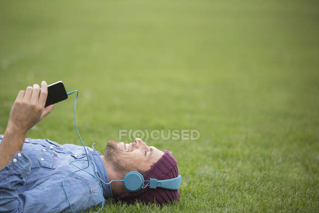 Счастливый молодой человек слушает наушники на лужайке — стоковое фото