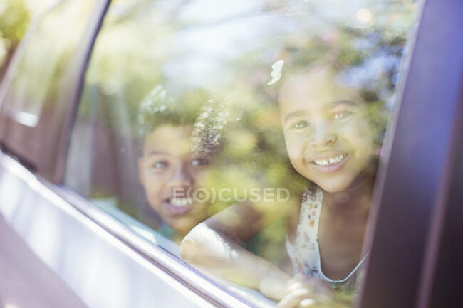 Portrait of happy brother and sister looking out car window — Stock Photo