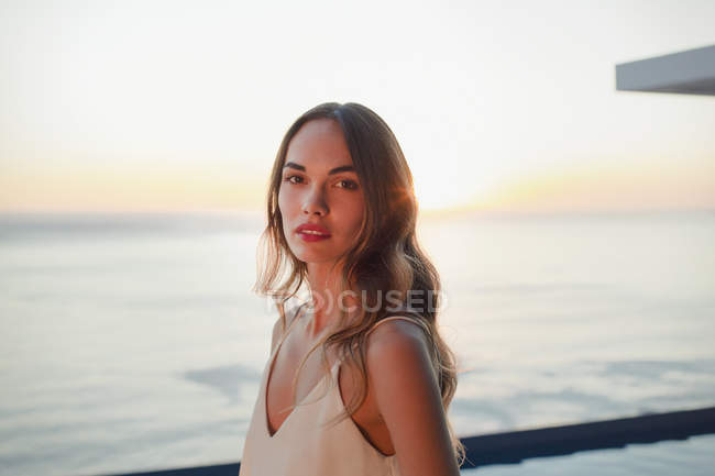 Portrait serious, beautiful woman on luxury patio with sunset ocean view — Stock Photo
