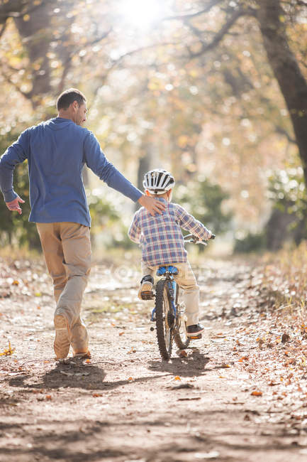 Отец учит сына ездить на велосипеде по дорожке в лесу — стоковое фото