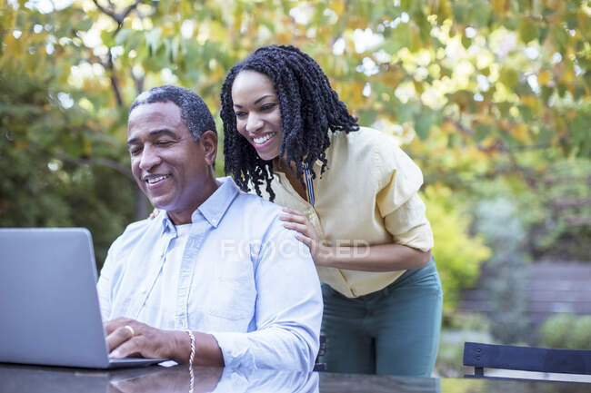 Padre e hija utilizando la computadora portátil en la mesa de patio - foto de stock