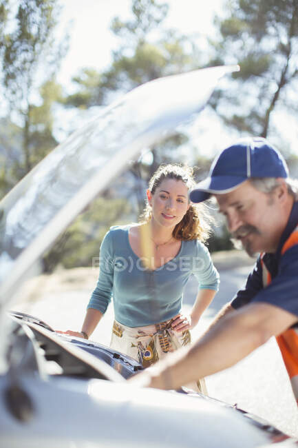 Женщина смотрит придорожный механик проверить двигатель автомобиля — стоковое фото
