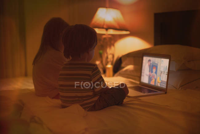 Boy and girl brother and sister watching video on laptop on bed — Stock Photo
