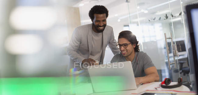 Sonrientes hombres de negocios creativos que trabajan en la computadora portátil en la oficina - foto de stock