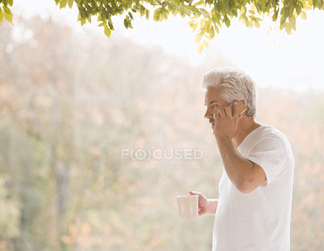 Man talking on cell phone and drinking coffee on autumn patio — Stock Photo