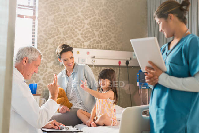 Doctor making rounds, gesturing with girl patient in hospital room — Stock Photo