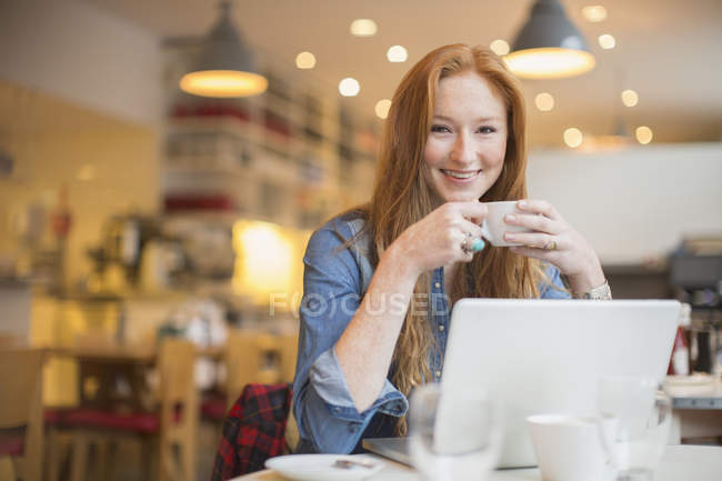Щаслива молода жінка використовує ноутбук у кафе — стокове фото