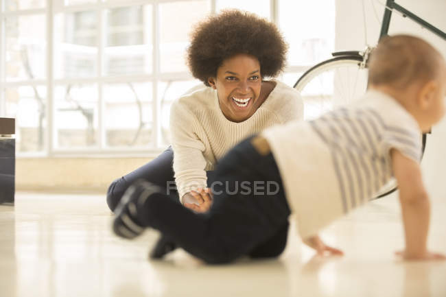 Мама смотрит, как мальчик ползает по полу в гостиной дома — стоковое фото