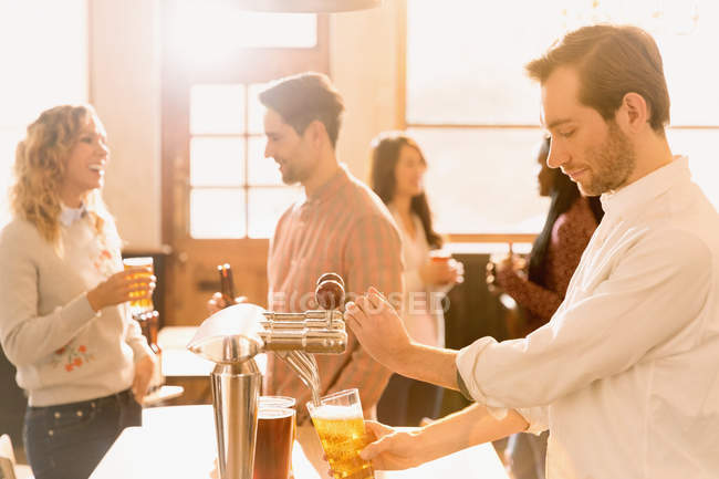 Bartender pouring beer at beer tap behind bar — Stock Photo