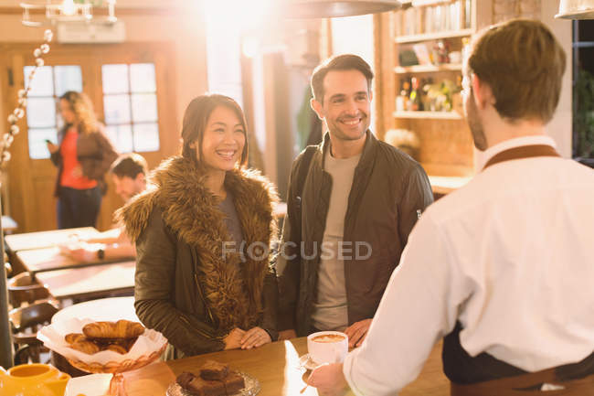 Barista sirve café a la pareja en el mostrador en la cafetería - foto de stock