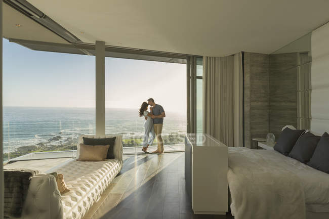 Affettuosa coppia che abbraccia il moderno balcone della camera da letto vetrina di lusso con vista sull'oceano — Foto stock