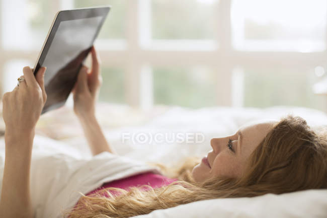 Жінка лежить в ліжку за допомогою цифрового планшета — стокове фото