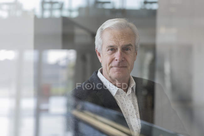 Ritratto fiducioso anziano uomo d'affari alla finestra presso l'ufficio moderno — Foto stock