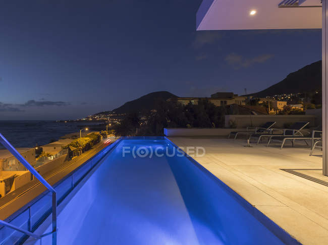 Illuminated blue lap swimming pool on luxury patio at night — Stock Photo
