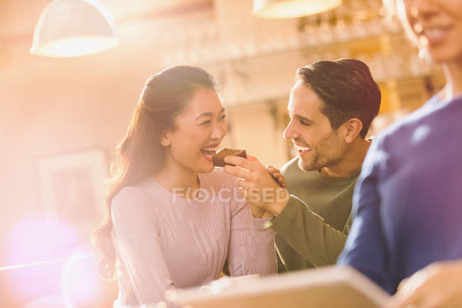 Playful boyfriend feeding brownie to girlfriend at cafe — Stock Photo