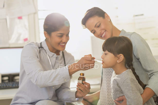 Pediatra hembra alimentando jarabe para la tos a paciente niña en sala de examen - foto de stock