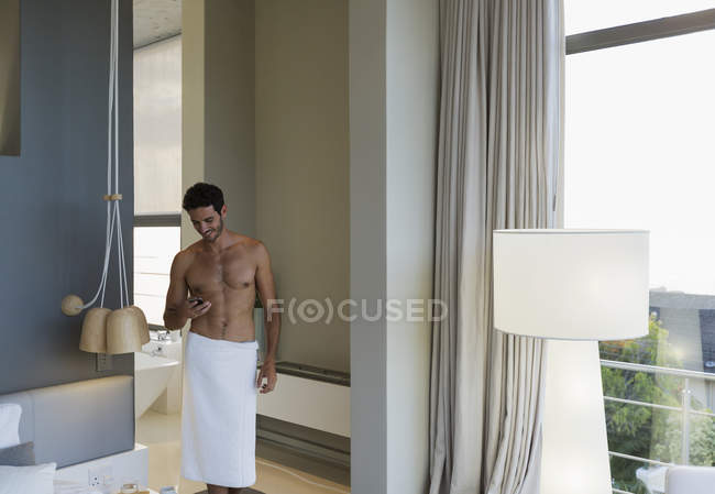 Man in towel texting with cell phone in bedroom — Stock Photo