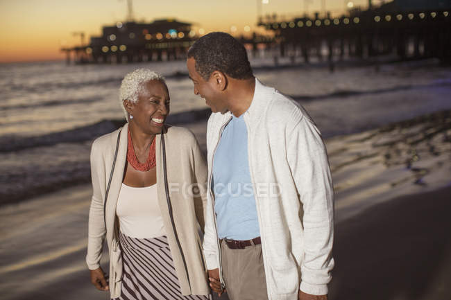 Seniorenpaar spaziert bei Sonnenuntergang am Strand — Stockfoto