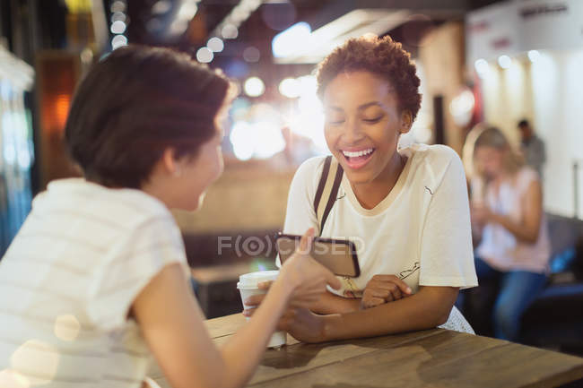 Young women friends using cell phone in cafe — Stock Photo