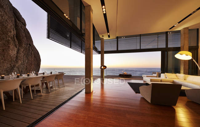 Modern luxury living room open to patio with sunset ocean view — Stock Photo