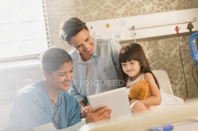 Female nurse showing digital tablet to girl patient and mother in hospital room — Stock Photo