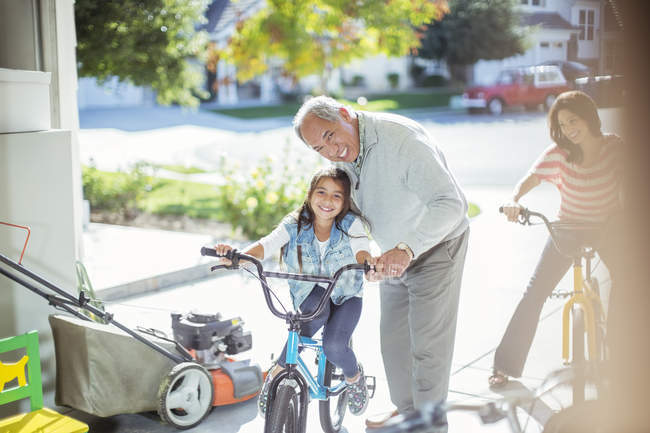 Grandfather and granddaughter on bike in garage — Stock Photo