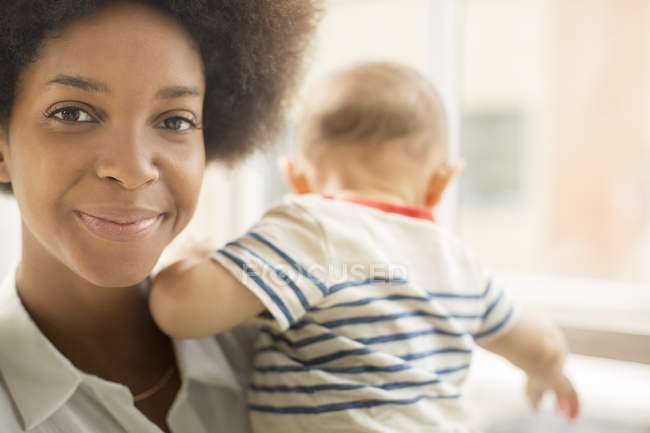 Smiling mother holding baby boy and looking at camera — Stock Photo