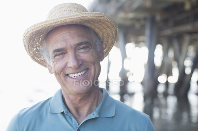 Retrato de hombre mayor sonriente en sombrero de sol en la playa - foto de stock