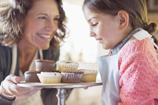 Feliz abuela ofreciendo cupcakes nieta - foto de stock