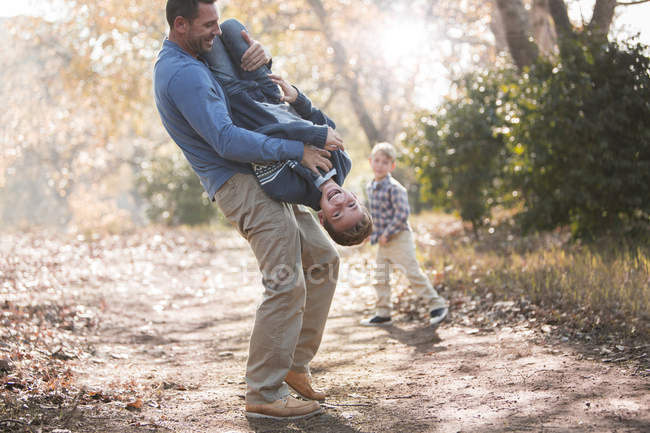 Playful father lifting son upside-down on path in woods — Stock Photo