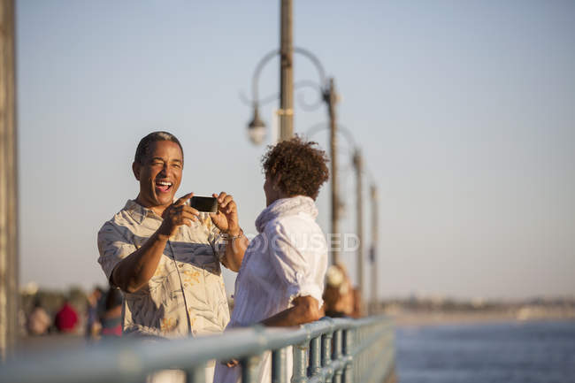 Hombre fotografiando mujer en muelle - foto de stock