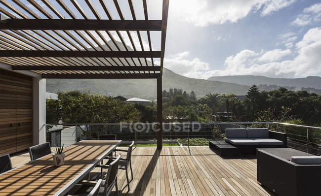 Солнечная современная витрина роскошного дома с деревянной палубой и видом на горы — стоковое фото