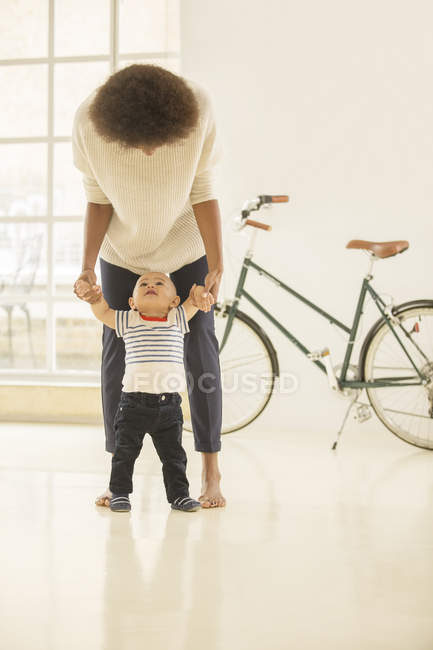 Mother helping baby boy walk in living room at home — Stock Photo