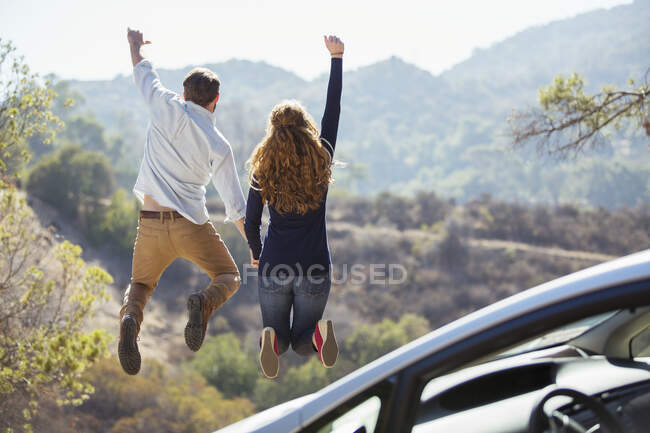 Enthusiastic couple jumping for joy outside car — Stock Photo