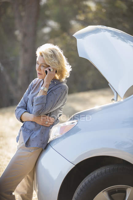 Woman talking on cell phone with automobile hood raised at roadside — Stock Photo
