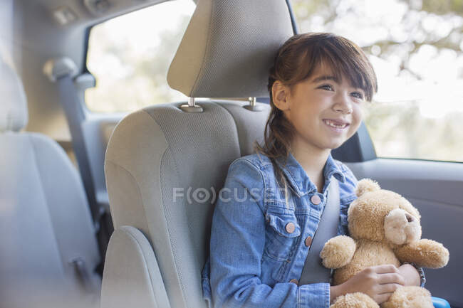 Menina feliz com ursinho de pelúcia no banco de trás do carro — Fotografia de Stock