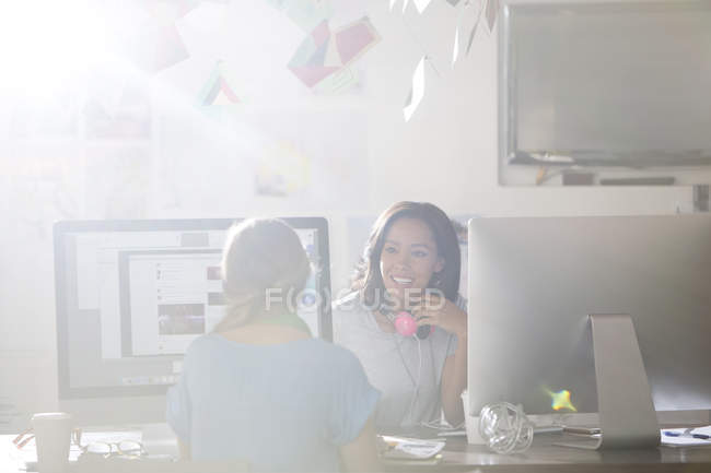 Creative businesswoman with headphones talking at computers in sunny office — Stock Photo