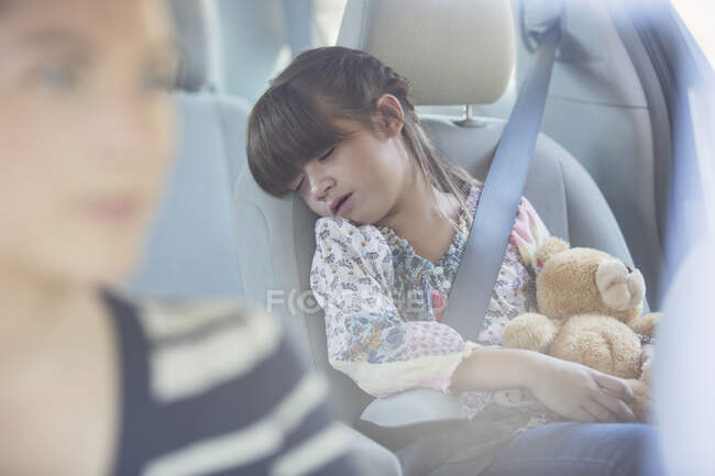 Fille avec ours en peluche dormant sur le siège arrière de la voiture — Photo de stock