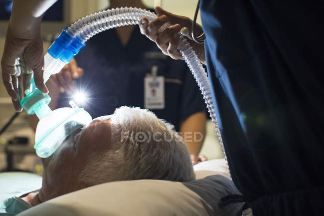 Médico femenino usando máscara mientras anestesiaba a paciente anciano en cirugía - foto de stock