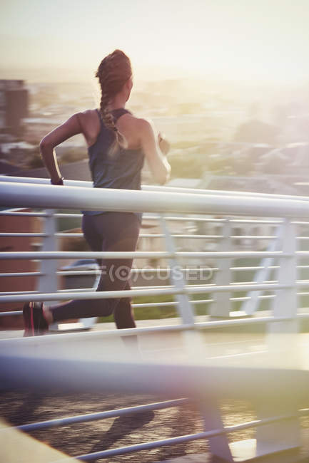 Жінка біжить на сонячному міському пішохідному мосту на сході сонця — стокове фото