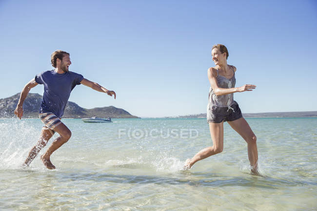 Coppia che corre in onde sulla spiaggia — Foto stock