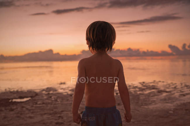 Хлопчик на пляжі дивиться на спокійний захід сонця океан — стокове фото