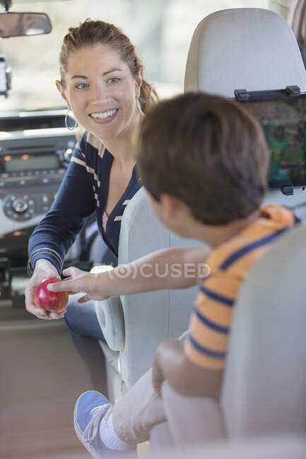 Madre dando chico una manzana dentro de coche - foto de stock