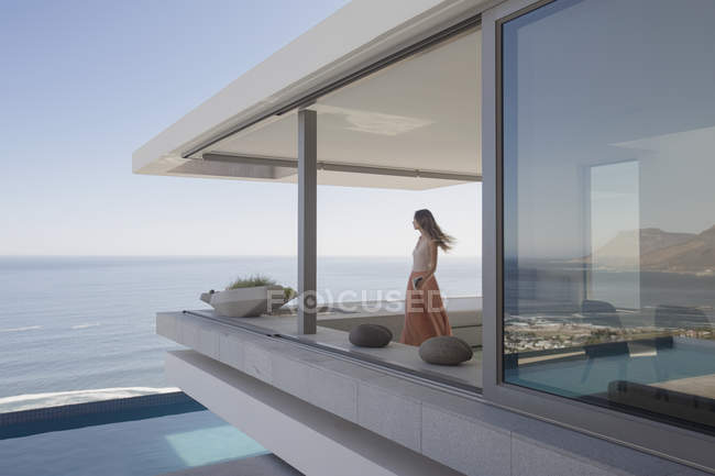 Жінка дивиться на океанський вид на сучасний, розкішний будинок вітрина зовнішній балкон — стокове фото