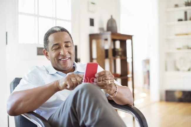 Mensagens de texto homem sênior com telefone celular na sala de estar — Fotografia de Stock