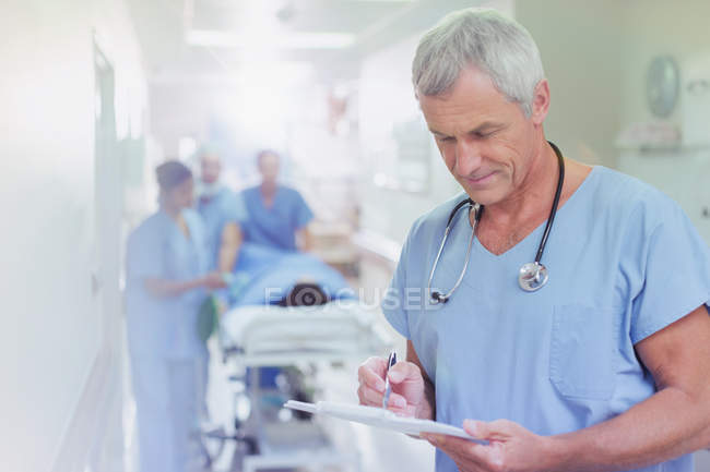 Mature male surgeon reviewing medical record clipboard in hospital corridor — Stock Photo
