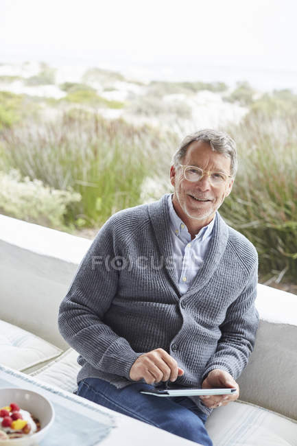 Porträt lächelnder älterer Mann mit digitalem Tablet auf Strandterrasse — Stockfoto